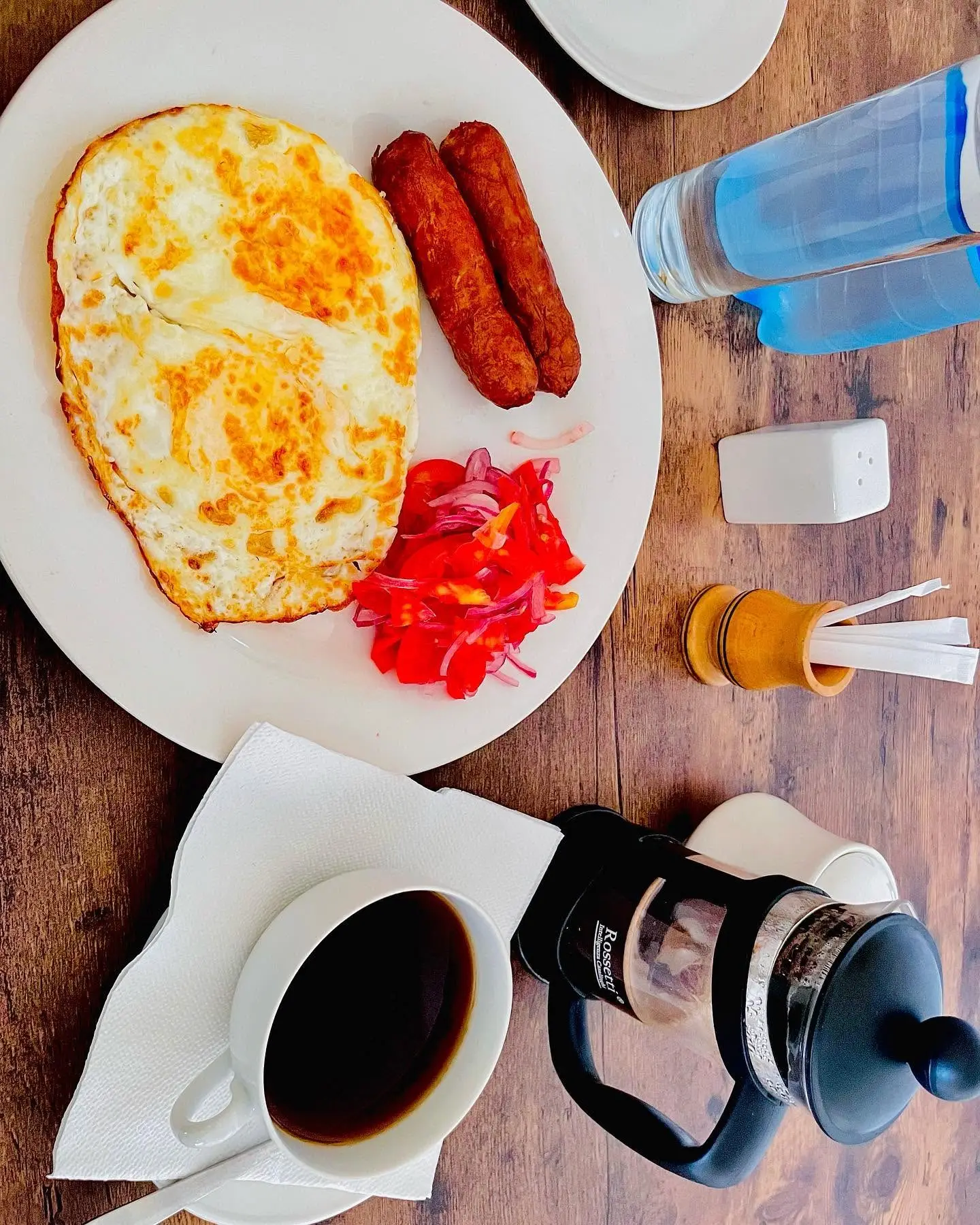 Fried eggs, sausages, kachumbari and a French press of coffee on a wooden table